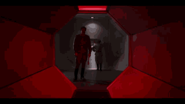 a man is standing in a dark room with red lights behind him