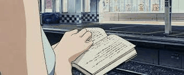 a person is reading a book while sitting on a train platform .