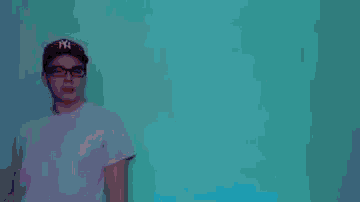 a young man wearing a red hat and glasses is dancing in front of a blue background .