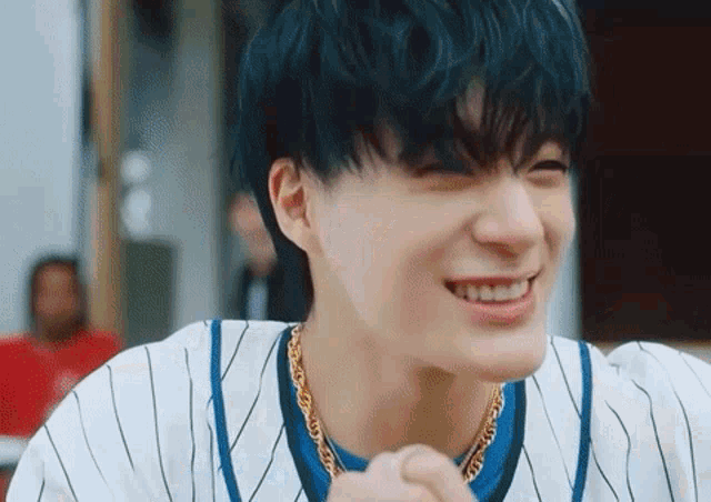 a young man with blue hair is wearing a striped shirt and a gold chain .