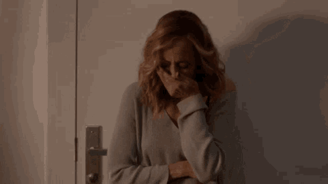 a woman is standing in front of a door covering her face with her hands .