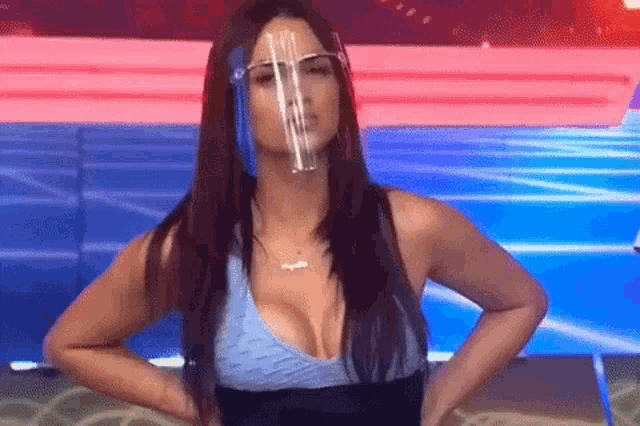 a woman wearing a face shield and a blue top is standing on a stage with her hands on her hips .
