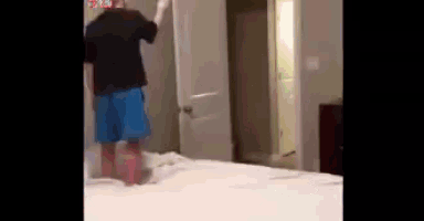 a man in a black shirt and blue shorts is jumping on a bed in a bedroom .