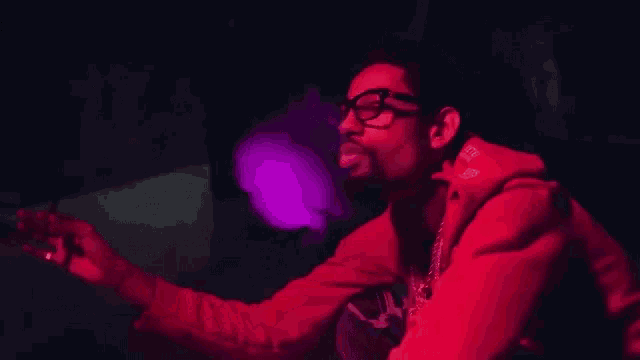 a man wearing glasses and a red jacket is smoking a cigarette in a dark room .