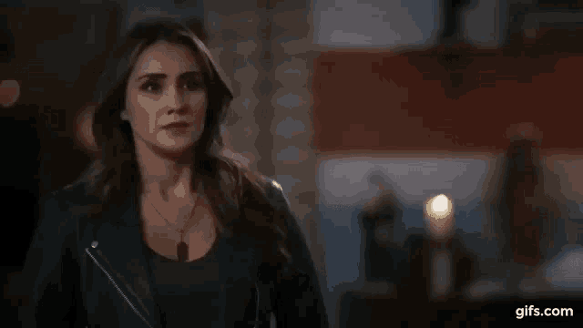 a woman in a leather jacket and necklace is standing in a room .