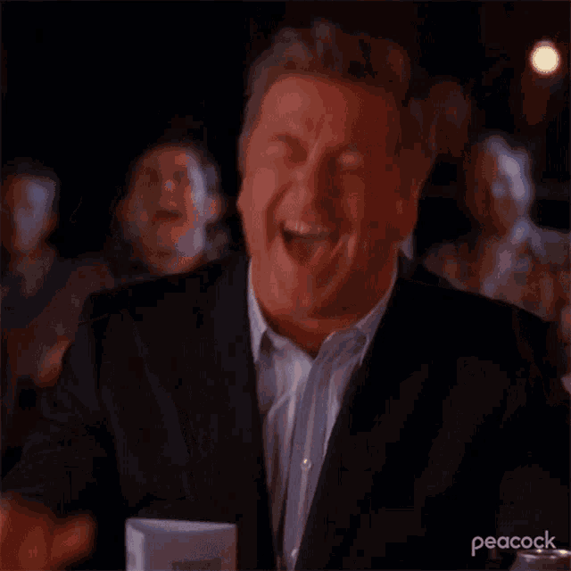 a man in a suit is laughing in front of a crowd .