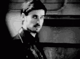 a man with a beard is wearing a leather jacket and looking at the camera in a black and white photo .