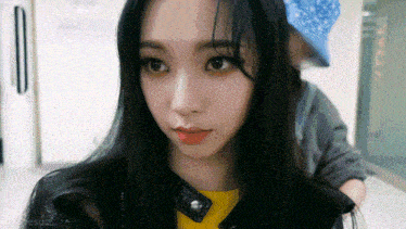a woman with long black hair is wearing a yellow shirt and a black leather jacket .