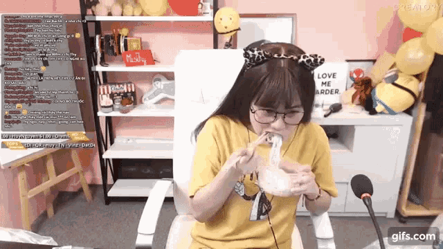 a girl wearing glasses and a yellow shirt is sitting in front of a microphone with a sign that says love me order on it