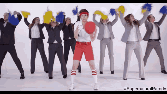 a group of people in suits are dancing with a woman in red shorts holding a ball