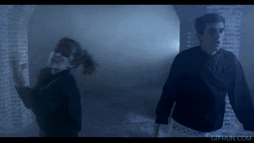 a man and a woman are standing in a dark room with a gifrun.com watermark