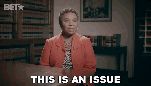 a woman sitting at a table with the words " this is an issue " on the screen