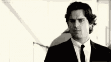 a man in a suit and tie is standing in front of a mirror and looking at himself .