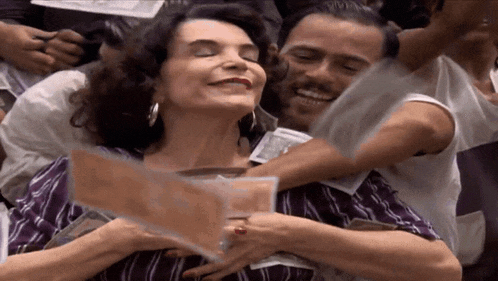 a man is hugging a woman who is smiling and holding a piece of paper