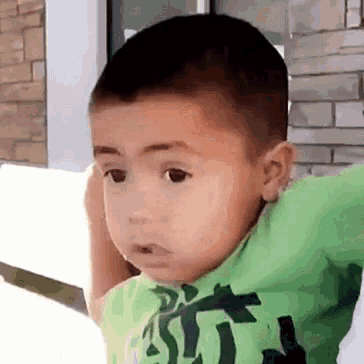 a young boy wearing a green shirt is covering his ears with his hand .