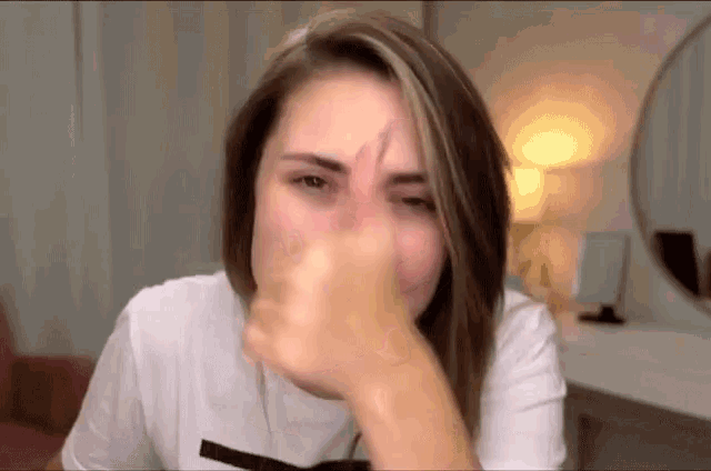 a woman in a white t-shirt is covering her nose with her hand .