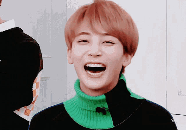 a young man wearing a green sweater is laughing with his mouth wide open