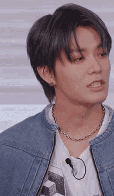 a young man wearing a denim jacket and a necklace with a microphone attached to it