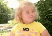 a little girl in a yellow shirt with the word true on it .
