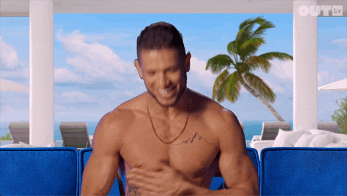 a shirtless man is sitting on a blue couch with out tv written on the bottom right