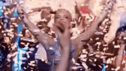 a woman is dancing in a crowd of people surrounded by confetti and holding her arms in the air .