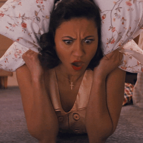 a woman wearing a necklace with a cross on it holds a pillow over her head