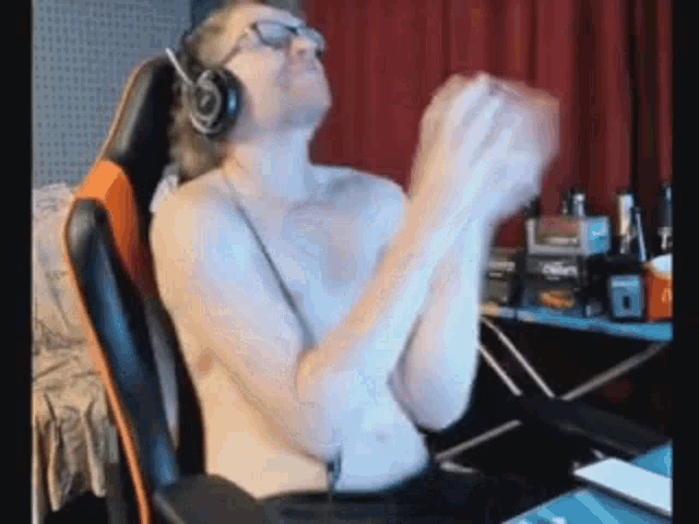 a shirtless man wearing headphones and glasses is sitting in a gaming chair .