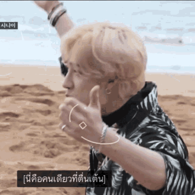 a man with blonde hair is giving a thumbs up on a beach .