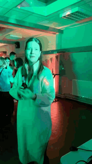 a woman holding a bottle of beer in a dark room with green lights