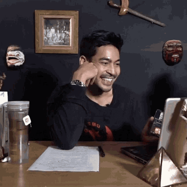 a man wearing a shirt that says ' smo ' on it sits at a desk