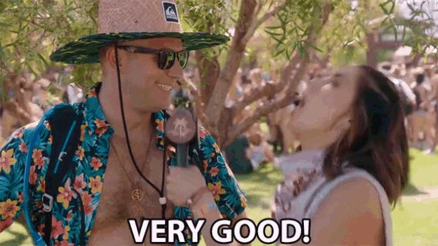a man wearing a straw hat and sunglasses is talking to a woman while holding a microphone and saying very good
