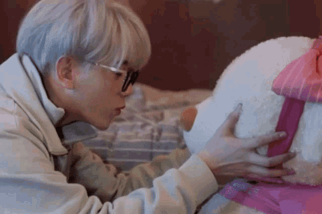 a man with glasses is holding a stuffed animal with a pink bow on it .
