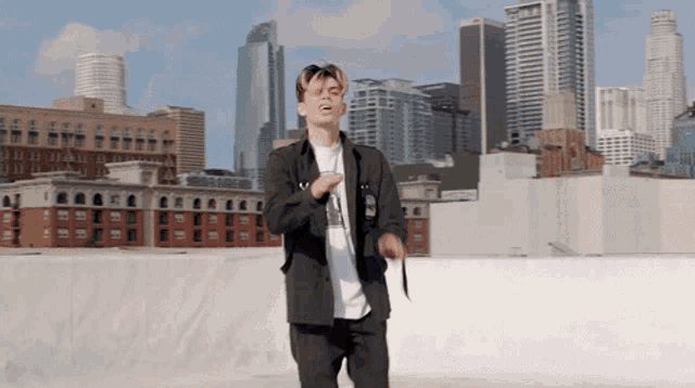 a man is standing on a rooftop with a city skyline behind him