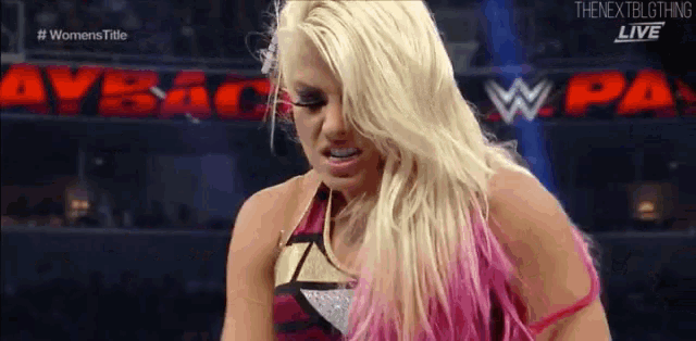 a woman with blonde hair and pink hair is standing in front of a sign that says ' women 's title '