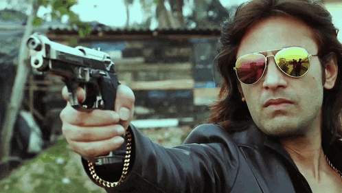 a man wearing sunglasses holds a gun in his right hand