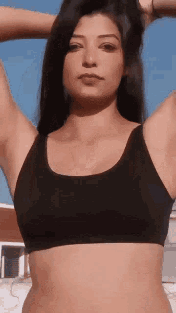 a woman in a black sports bra is holding her hair up in the air .
