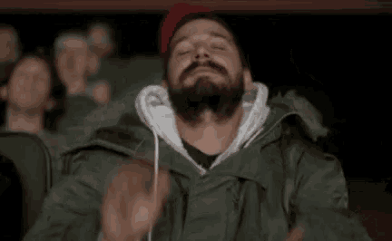 a man with a mustache is clapping his hands while sitting in a theater .