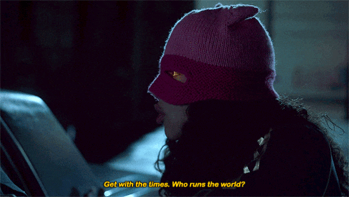 a woman wearing a pink mask is asking " get with the times who runs the world "