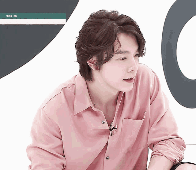 a man in a pink shirt is sitting in front of a sign that says ' oes mi '