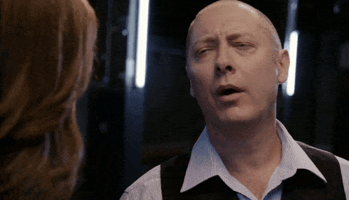 a man in a vest and striped shirt is talking to a woman in a dark room