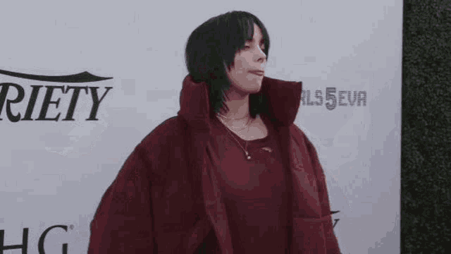 billie eilish is wearing a red jacket and a necklace on the red carpet .