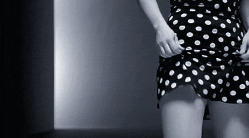 a woman in a black and white polka dot dress is adjusting her skirt