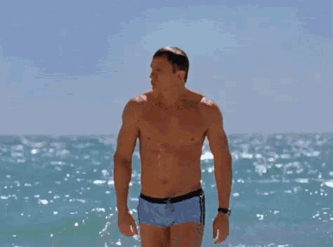 a shirtless man in blue swim trunks is standing on a beach .