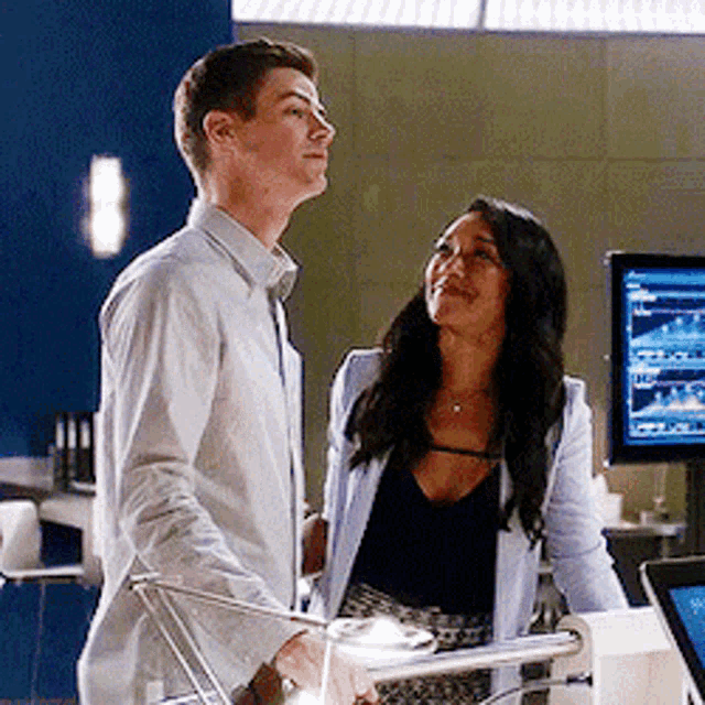 a man and a woman are standing in front of a computer monitor .