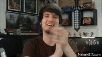 a man with a beard is clapping his hands in front of a wall with pictures on it .