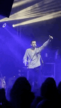 a man is singing into a microphone on a stage in front of a crowd of people .