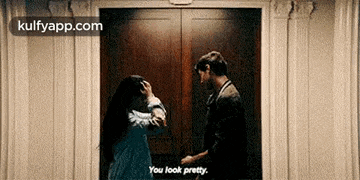 a man and a woman are standing next to each other in an elevator and the woman is holding the man 's hand .