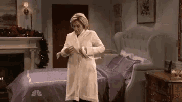 a woman in a white robe is standing in a bedroom next to a bed .