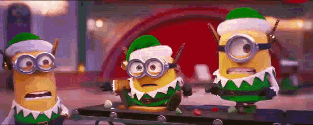 three minions dressed as elves are standing next to each other on a table .