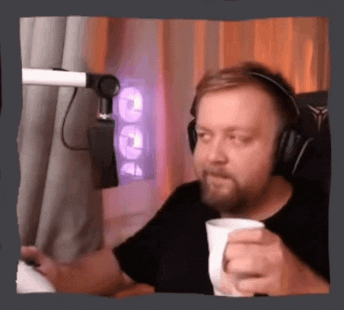 a man wearing headphones is sitting in front of a microphone holding a cup .